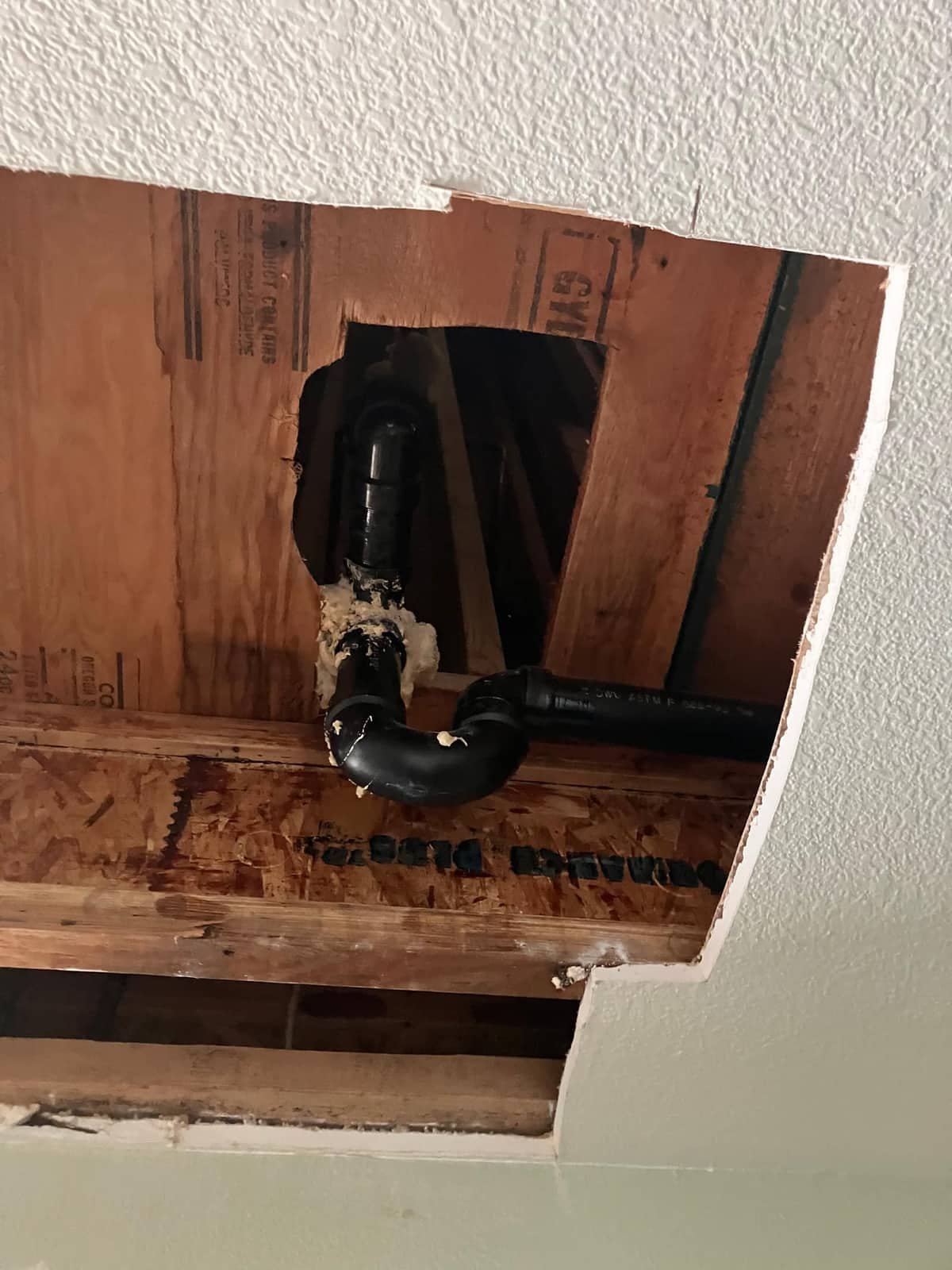 Drywall access hole cut to reach a drain pipe fitting for repair